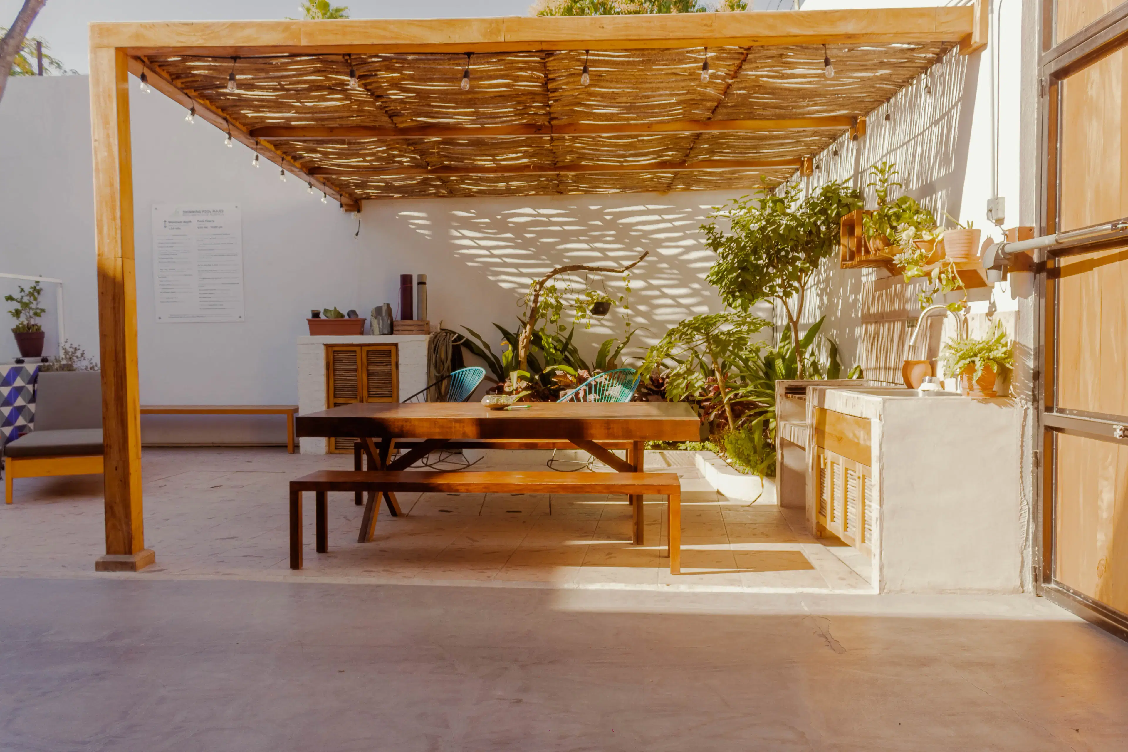 Outdoor pergola dining area with turquoise chairs and kitchenette